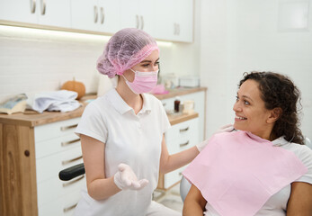 Dentist hygienist, dental assistant wearing pink medical mask and surgical gloves preparing woman...