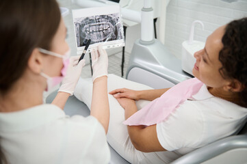 Focus on a dental X-ray in hands of dentist showing the jaw and teeth and discussing with a patient during dental examination, explaining the consultations treatment issues. Diagnostics in dentistry