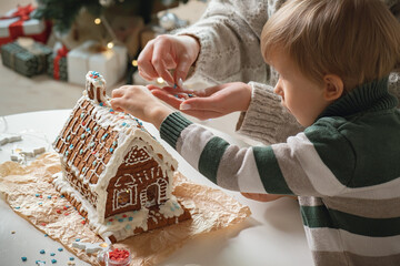 Little boy with mom decorating christmas gingerbread house together, family activities and...