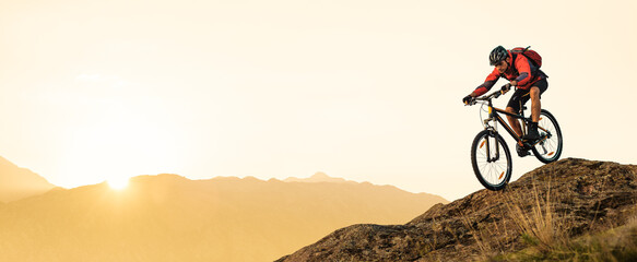 Cyclist Riding Bike on the Rocky Trail in the Summer Mountains at Sunset. Extreme Sport and Enduro Cycling Concept. - obrazy, fototapety, plakaty