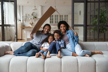 Happy African American couple and two kids holding cardboard roof over heads, imitating house....