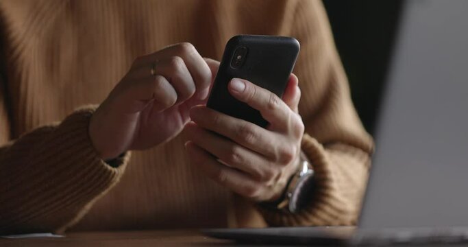 Close up shot of man hands with watch using mobile phone while working at laptop. Male fingers typing and tapping on smartphone. Texting and scrolling. Slow motion.