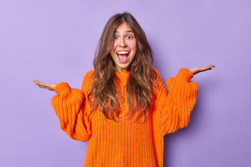 Indoor shot of happy emotional woman with long hair raises palms exclaims from joy wears casual...