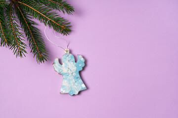 A blue angel hangs on a spruce branch. Epoxy resin christmas tree decorations on purple background with copy space.