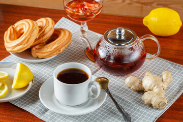 A teapot and a cup of strong aromatic tea on the table on a napkin next to ginger and lemon jam and donuts.