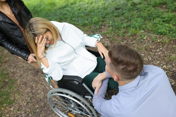 Young disabled woman in wheelchair crying near man sitting in front of her in park