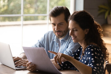 Reading documents. Family couple study papers search information by loan mortgage affordable housing program on website. Young spouses clients hold bank account statement check financial data online