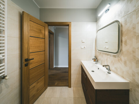 Modern interior of bathroom. White sink. Wooden door with tile floor.