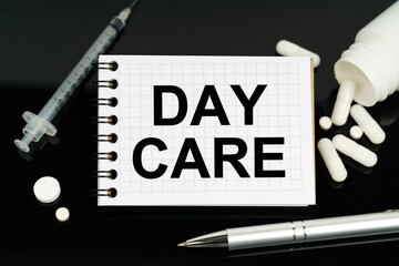 On the black surface are pills, a syringe and a notebook with the inscription - day care