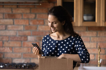 Young hispanic woman blogger unpack postal delivery container using mobile phone camera to film...
