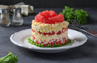Festive salad with grapefruit, cheese and crab sticks on a white plate on a gray background