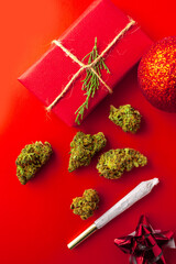 Christmas cannabis theme of marijuana buds on red background with joint and present gift wrapped