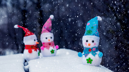Cheerful snowmen in the woods in the snow on a dark background during a snowfall