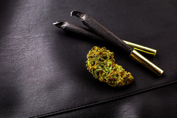 Cannabis bud and marijuana joints on black leather background