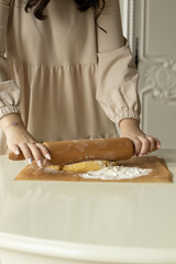 A girl rolls out the dough on parchment paper sprinkled with flour with a wooden rolling pin.