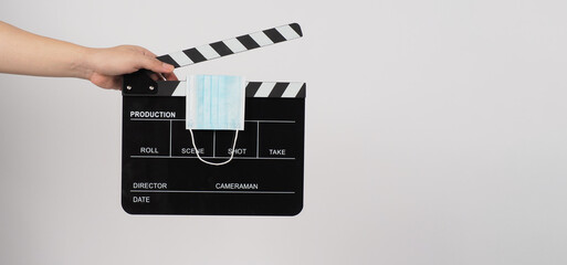 Fototapeta na wymiar Hand is holding Clapperboard or movie slate and face mask on white background.
