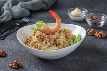 Salad with shrimps, pineapple, olives and walnuts in a white plate on a dark gray background. Festive snack