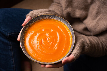 Female hands holding plate with thanksgiving pumpkin cream soup.