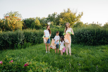 A group of girls with children at sunset are engaged in garbage collection in the park. Environmental care, recycling.