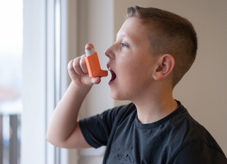 Fototapeta premium Young boy using asthma inhaler at home