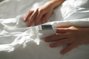 The teenager lies in bed and measure the oxygen saturation with a pulse oximeter. Asthma treatment. The sick child lies in bed. Bedroom or hospital room for a small patient.