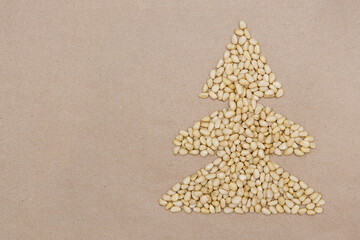 Pine nuts are laid out on a plain craft background in the shape of a Christmas tree. Christmas style.