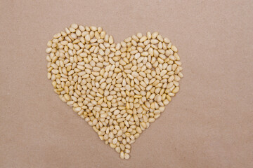 Pine nuts are laid out on a solid craft background in the shape of a heart. The concept of healthy eating.