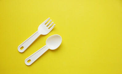 Fork and spoon on a yellow background. Plastic utensils. Tableware for games. Meals, lunch. Children is set of dishes. Top view. Copy space