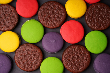 Colorful macarounds and round chocolate chip cookies are laid out on a dark background.