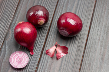 Three purple onion heads, sliced onions into rings and husks on table.