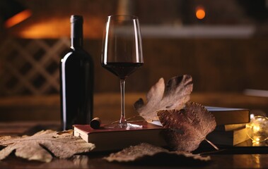Glass of red wine, book with autumn leaves on table. Dark and warm colors.
