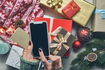 Top view of woman using phone for online shopping on Christmas background with gift boxes and...