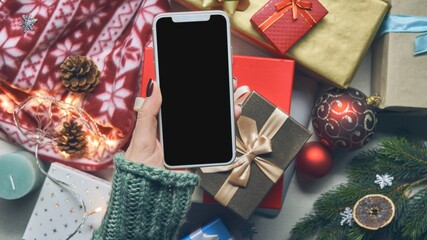 Top view of woman holding phone on Christmas background with gift boxes and Christmas decorations....