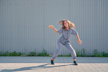 Dancing teen girl happy rhythmically moving against textured street fence. Energetic cool teen female dancer having fun