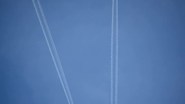High flying airplanes jet leaves a contrail. Passenger commercial planes cross each other against blue cloudless sky leaving water vapor contrails behind as seen from the ground. Aircraft passing by