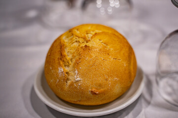 Pan sobre en la mesa de un restaurante con mantel de tela blanco, sobre un pequeño plato.