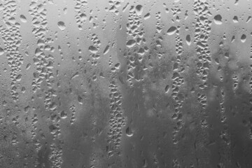 Raindrops on the window pane on a gray background. Natural pattern of raindrops. Texture for creativity. Water on the surface of the glass.