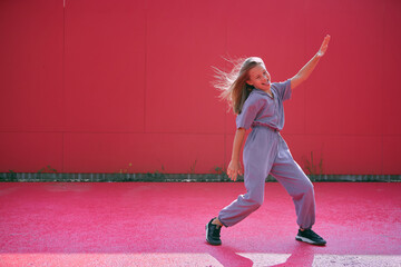 Happy teen girl dancing having fun outdoors on red background. Joyful young female dancer perform modern dance