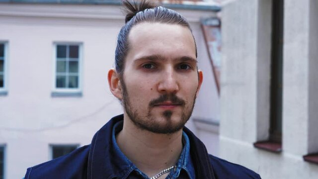 Portrait of handsome urban hispanic man with beard and ponytail outdoors. Confident Latin american guy looking at camera outdoors