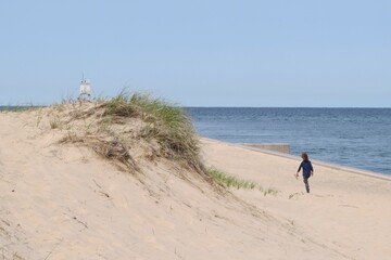 Fototapeta na wymiar Girl Walking along Sandy Beach of Lake Superior toward Grand Marais Range Light