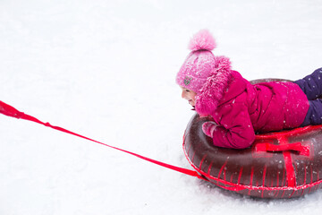 A girl rides a tube from a slide in winter in a snowfall. Tubing, winter sports outdoor and family...