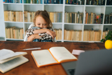 Front view of overwhelmed upset primary child school girl sitting alone hugging knees in front of...