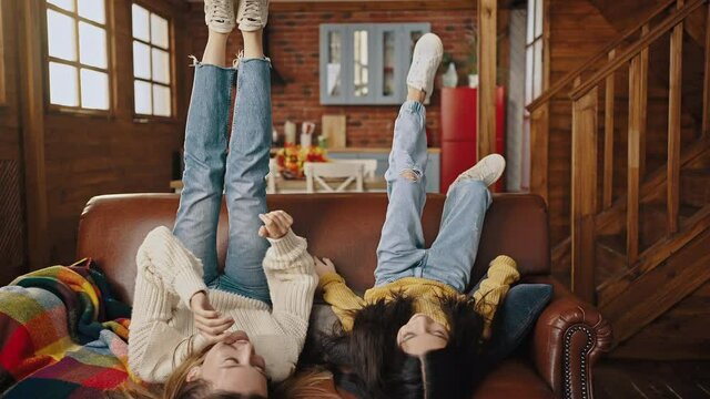 Mother and little daughter falling down on couch with their feet up, laughing, tickling each other. Kitchen of country house. Close up, slow motion