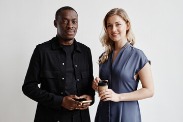 Minimal waist up portrait of two modern business people looking at camera while standing by white wall, copy space