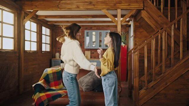 Young mum and little daughter laughing, dancing, whirling and tickling while having fun in kitchen of wooden country house. Slow motion