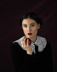 Studio portrait of pretty woman dark hair, white collar. Face, Thinking. Hold red apple. Dark background