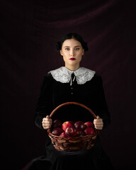 Model in gothic costume on a black background. The girl is holding a red apple as symbol of temptation
