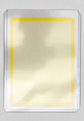 blank trading card mock up with yellow border behind transparent plastic top loader case on white paper background.