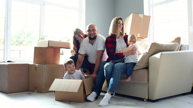 Happy family of five sitting at the sofa among boxes against big windows and smiling. Removing concept.