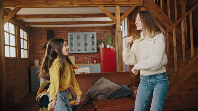 Young mom and little daughter laughing, dancing, falling down on sofa being tired. Having fun in kitchen of country house. Close up, slow motion